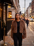 Woman wearing cropped brown faux fur jacket on evening city street, lifestyle