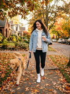 Woman wearing oversized denim jacket walking a dog in autumn