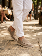 Man wearing beige suede laceless loafers on a sunlit street